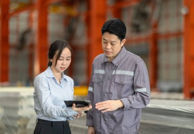 Profesyonel bir erkek ve kadın dijital tablet üzerinde iş birliği yaparak, sürdürülebilir iyileştirme için ISO standartlarını yükseltmek için bir metal levha fabrikasının hareketli ortamında iş birliği yapıyorlar..