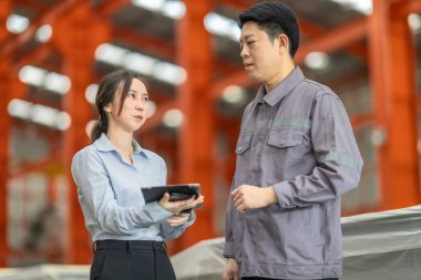 Profesyonel bir erkek ve kadın dijital tablet üzerinde iş birliği yaparak, sürdürülebilir iyileştirme için ISO standartlarını yükseltmek için bir metal levha fabrikasının hareketli ortamında iş birliği yapıyorlar..