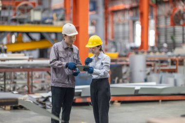 Profesyonel bir erkek ve kadın dijital tablet üzerinde iş birliği yaparak, sürdürülebilir iyileştirme için ISO standartlarını yükseltmek için bir metal levha fabrikasının hareketli ortamında iş birliği yapıyorlar..