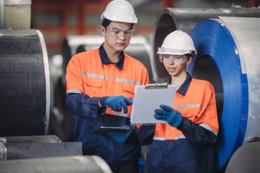 Bir erkek ve kadın mühendis titiz bir envanter denetimi yapıyor, bir metal levha fabrikasının depolama alanından geçiyor, hisse senedi doğruluğu ve üretime hazır olmasını sağlıyor.