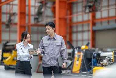 İki profesyonel, bir erkek ve bir kadın, yoğun bir metal işleme fabrikasında yürürken, takım çalışması ve sanayi uzmanlığını ön plana çıkararak işletim süreçlerini tartışıyor. CO2 emisyonları optimize ediliyor.