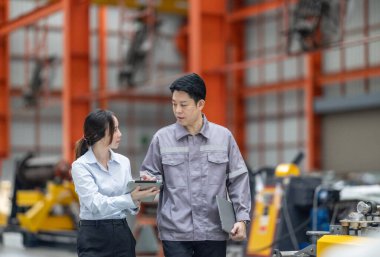 İki profesyonel, bir erkek ve bir kadın, yoğun bir metal işleme fabrikasında yürürken, takım çalışması ve sanayi uzmanlığını ön plana çıkararak işletim süreçlerini tartışıyor. CO2 emisyonları optimize ediliyor.