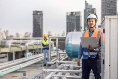 Profesyonel sanayi mühendisi, dizüstü bilgisayarla donatılmış, modern bir tesisin karmaşık boru hattı altyapısı içinde titizlikle bir HVAC sistemine sorun çıkarıyor. Karbon ayak izi azaltılıyor.