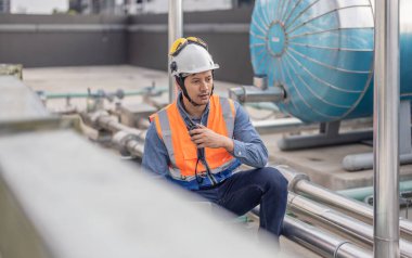 Profesyonel sanayi mühendisi, dizüstü bilgisayarla donatılmış, modern bir tesisin karmaşık boru hattı altyapısı içinde titizlikle bir HVAC sistemine sorun çıkarıyor. Karbon ayak izi azaltılıyor.