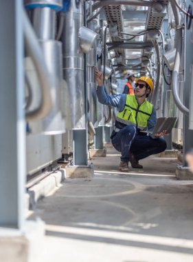 Profesyonel sanayi mühendisi, dizüstü bilgisayarla donatılmış, modern bir tesisin karmaşık boru hattı altyapısı içinde titizlikle bir HVAC sistemine sorun çıkarıyor. Karbon ayak izi azaltılıyor.