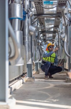 Profesyonel sanayi mühendisi, dizüstü bilgisayarla donatılmış, modern bir tesisin karmaşık boru hattı altyapısı içinde titizlikle bir HVAC sistemine sorun çıkarıyor. Karbon ayak izi azaltılıyor.