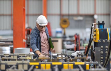 Deneyimli bir yönetici, metal levha fabrikasının mekanizmaları arasında kalite kontrolü yaparken bir tabletteki verileri titizlikle inceler.