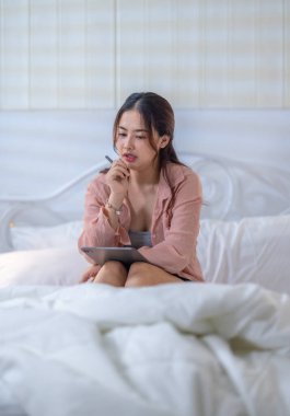 Genç bir kadın rahat yatak odasında tablet kullanırken yaratıcı düşüncelere daldı. Bir ilham ve üretkenlik anını resmediyordu.