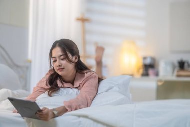 Genç bir kadın rahat yatak odasında tablet kullanırken yaratıcı düşüncelere daldı. Bir ilham ve üretkenlik anını resmediyordu.