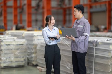 Metal fabrikasındaki stratejik planlama oturumunda çalışan bir erkek ve kadın arasında dijital aletlerin iş akışını artırdığı odaklı bir etkileşim.