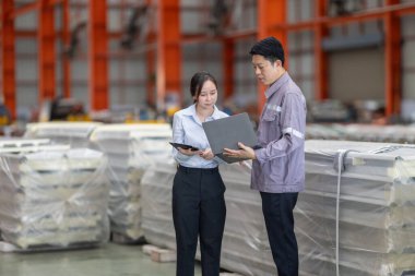 Metal fabrikasındaki stratejik planlama oturumunda çalışan bir erkek ve kadın arasında dijital aletlerin iş akışını artırdığı odaklı bir etkileşim.