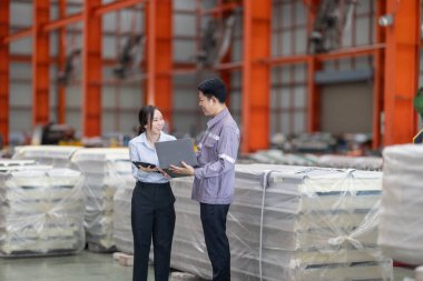 Metal fabrikasındaki stratejik planlama oturumunda çalışan bir erkek ve kadın arasında dijital aletlerin iş akışını artırdığı odaklı bir etkileşim.