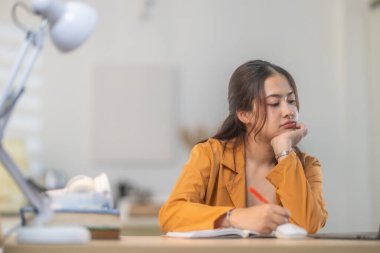 Günümüz ev ofisinin düzenli masasında dizüstü bilgisayar üzerinde çalışan sarı ceketli genç bir kadın. Görüntü üretkenliği, odaklanmayı ve ev ortamında rahat bir çalışma sunar..