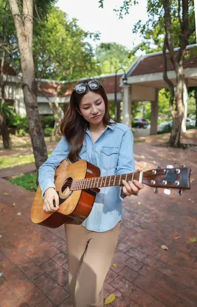 Genç bir kadın halka açık alanda akustik gitar çalıyor, müziğe dalmış. Serin açık hava ortamı sakin ve sanatsal atmosfere katkı sağlayarak yaratıcı enerji ve performans için mükemmel bir zemin oluşturur..