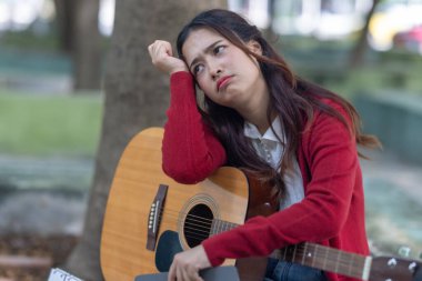 Genç bir kadın halka açık alanda akustik gitar çalıyor, müziğe dalmış. Serin açık hava ortamı sakin ve sanatsal atmosfere katkı sağlayarak yaratıcı enerji ve performans için mükemmel bir zemin oluşturur..