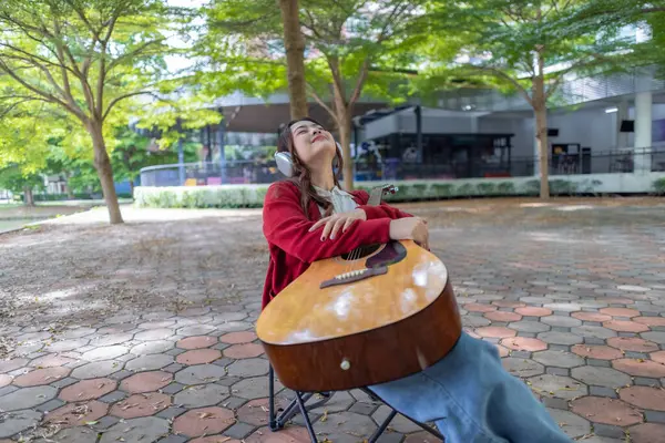 Genç bir kadın halka açık alanda akustik gitar çalıyor, müziğe dalmış. Serin açık hava ortamı sakin ve sanatsal atmosfere katkı sağlayarak yaratıcı enerji ve performans için mükemmel bir zemin oluşturur..