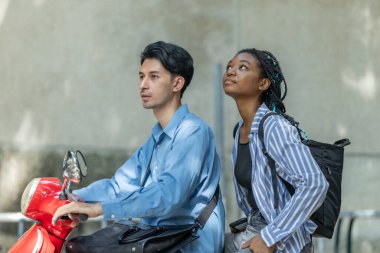 İki genç profesyonel elektrikli bir motosikletle şehir ortamında sürdürülebilir ve çevre dostu bir seyahati teşvik ederek işe gidip geliyor. Görüntü modern ulaşım ve takım çalışmasını vurguluyor.