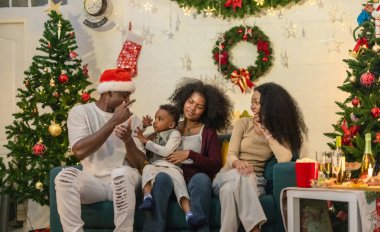 Siyah aile rahat bir kanepede toplanmış, Noel kutlamalarında abur cubur ve içeceklerin keyfini çıkarıyordu. Süslü Noel ağaçları, çoraplar, çelenkler, bayram neşesinin özünü yakalama.