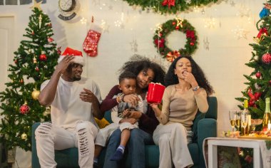 Siyah aile rahat bir kanepede toplanmış, Noel kutlamalarında abur cubur ve içeceklerin keyfini çıkarıyordu. Süslü Noel ağaçları, çoraplar, çelenkler, bayram neşesinin özünü yakalama.