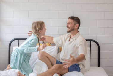 A man and his daughter are embracing on a bed covered with white sheets. The room is bright, and they both share smiles, creating a warm family atmosphere on a peaceful morning. clipart