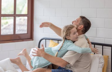 A man and his daughter are embracing on a bed covered with white sheets. The room is bright, and they both share smiles, creating a warm family atmosphere on a peaceful morning. clipart