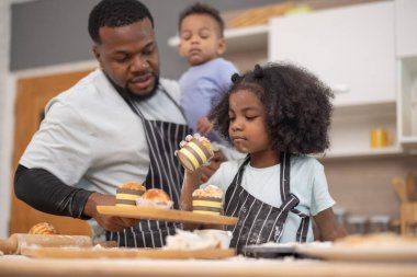 Bir baba ve iki çocuğu sıcak bir mutfakta yemek hazırlıyorlar. İçindekileri karıştırıyor ve un ile kaplanmışken eğleniyorlar. Neşeli bağlılık anlarını resmediyorlar..