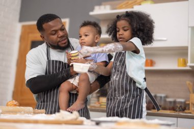 Bir baba ve iki çocuğu sıcak bir mutfakta yemek hazırlıyorlar. İçindekileri karıştırıyor ve un ile kaplanmışken eğleniyorlar. Neşeli bağlılık anlarını resmediyorlar..