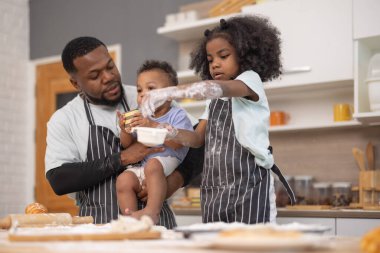 Bir baba ve iki çocuğu sıcak bir mutfakta yemek hazırlıyorlar. İçindekileri karıştırıyor ve un ile kaplanmışken eğleniyorlar. Neşeli bağlılık anlarını resmediyorlar..