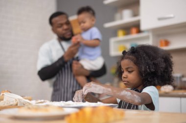 Bir baba ve iki çocuğu sıcak bir mutfakta yemek hazırlıyorlar. İçindekileri karıştırıyor ve un ile kaplanmışken eğleniyorlar. Neşeli bağlılık anlarını resmediyorlar..