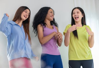 Üç kültürlü arkadaştan oluşan canlı bir grup içeride dans seansının keyfini çıkarıyor. Neşeli ve rahat görünüyorlar, günlük atletik kıyafetler giyiyorlar, arkadaşlığı, eğlenceyi ve hareketi vurguluyorlar.