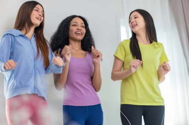 Üç kültürlü arkadaştan oluşan canlı bir grup içeride dans seansının keyfini çıkarıyor. Neşeli ve rahat görünüyorlar, günlük atletik kıyafetler giyiyorlar, arkadaşlığı, eğlenceyi ve hareketi vurguluyorlar.