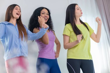 Üç kültürlü arkadaştan oluşan canlı bir grup içeride dans seansının keyfini çıkarıyor. Neşeli ve rahat görünüyorlar, günlük atletik kıyafetler giyiyorlar, arkadaşlığı, eğlenceyi ve hareketi vurguluyorlar.