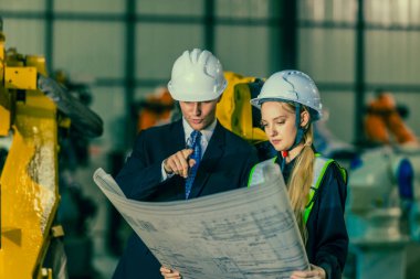 Kadın bir mühendis, robot endüstriyel ortamdaki bir müşteriye robot çözümler izah eder ve gösterir. Sahne, profesyonel bir ortamda yenilik, takım çalışması ve teknolojiyi ön plana çıkarıyor..