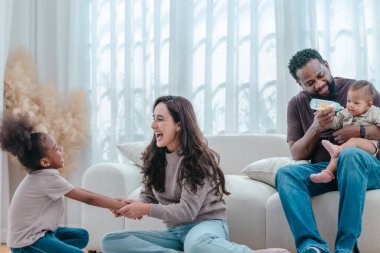 Çeşitli ailelerin birlikte oturma odasında kaliteli zaman geçirmesi çok iç açıcı bir manzara. Grupta ebeveynler ve iki çocuk, modern aile ortamında sevgi, bağlantı ve birliktelik sergileniyor.