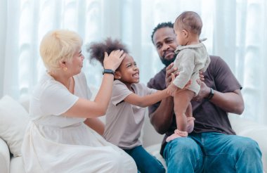Çeşitli ailelerin birlikte oturma odasında kaliteli zaman geçirmesi çok iç açıcı bir manzara. Grupta ebeveynler ve iki çocuk, modern aile ortamında sevgi, bağlantı ve birliktelik sergileniyor.