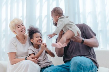 Çeşitli ailelerin birlikte oturma odasında kaliteli zaman geçirmesi çok iç açıcı bir manzara. Grupta ebeveynler ve iki çocuk, modern aile ortamında sevgi, bağlantı ve birliktelik sergileniyor.