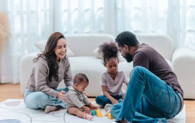 Çeşitli ailelerin birlikte oturma odasında kaliteli zaman geçirmesi çok iç açıcı bir manzara. Grupta ebeveynler ve iki çocuk, modern aile ortamında sevgi, bağlantı ve birliktelik sergileniyor.