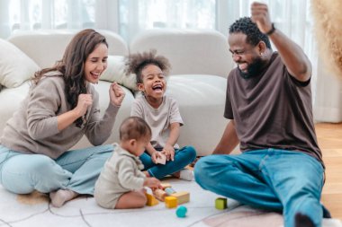Çeşitli ailelerin birlikte oturma odasında kaliteli zaman geçirmesi çok iç açıcı bir manzara. Grupta ebeveynler ve iki çocuk, modern aile ortamında sevgi, bağlantı ve birliktelik sergileniyor.