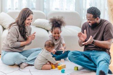Çeşitli ailelerin birlikte oturma odasında kaliteli zaman geçirmesi çok iç açıcı bir manzara. Grupta ebeveynler ve iki çocuk, modern aile ortamında sevgi, bağlantı ve birliktelik sergileniyor.