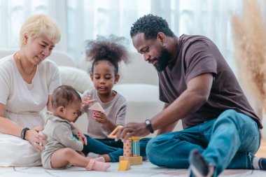 Çeşitli ailelerin birlikte oturma odasında kaliteli zaman geçirmesi çok iç açıcı bir manzara. Grupta ebeveynler ve iki çocuk, modern aile ortamında sevgi, bağlantı ve birliktelik sergileniyor.