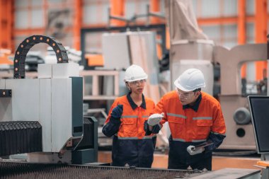 Metal levha fabrikasındaki iki mühendis lazer kesme makinesi üzerinde tartışıyorlar, teknik çizimleri inceliyorlar ve üretim özellikleriyle aynı hizayı sağlıyorlar..