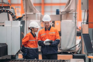 Metal levha fabrikasındaki iki mühendis lazer kesme makinesi üzerinde tartışıyorlar, teknik çizimleri inceliyorlar ve üretim özellikleriyle aynı hizayı sağlıyorlar..