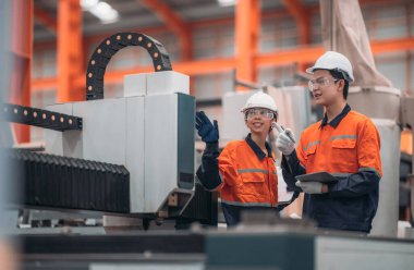 Metal levha fabrikasındaki iki mühendis lazer kesme makinesi üzerinde tartışıyorlar, teknik çizimleri inceliyorlar ve üretim özellikleriyle aynı hizayı sağlıyorlar..
