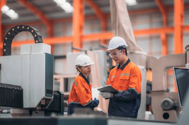 Metal levha fabrikasındaki iki mühendis lazer kesme makinesi üzerinde tartışıyorlar, teknik çizimleri inceliyorlar ve üretim özellikleriyle aynı hizayı sağlıyorlar..