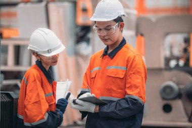 Metal levha fabrikasındaki iki mühendis lazer kesme makinesi üzerinde tartışıyorlar, teknik çizimleri inceliyorlar ve üretim özellikleriyle aynı hizayı sağlıyorlar..