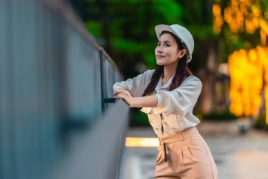 Beyaz güvenlik kaskı ve iş kıyafeti giyen Asyalı kadın mimar yeşil şehir ticari projelerini denetlerken elinde bir tablet tutuyor. Modern, sürdürülebilir ticari kalkınmayı vurgula
