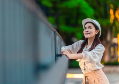 Beyaz güvenlik kaskı ve iş kıyafeti giyen Asyalı kadın mimar yeşil şehir ticari projelerini denetlerken elinde bir tablet tutuyor. Modern, sürdürülebilir ticari kalkınmayı vurgula