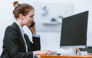 İş kadını, rapor üzerinde çalışırken masasında oturuyor. Modern ofis ortamı, bilgisayar ve düzenli çalışma alanı ile birlikte, verimliliği, verimliliği ve pozitif çalışma ortamını yansıtır..