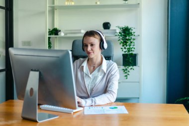 İş kadını, rapor üzerinde çalışırken masasında oturuyor. Modern ofis ortamı, bilgisayar ve düzenli çalışma alanı ile birlikte, verimliliği, verimliliği ve pozitif çalışma ortamını yansıtır..