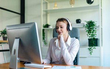 İş kadını, rapor üzerinde çalışırken masasında oturuyor. Modern ofis ortamı, bilgisayar ve düzenli çalışma alanı ile birlikte, verimliliği, verimliliği ve pozitif çalışma ortamını yansıtır..